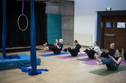 a large space, and several people on mats doing sit ups. There is also aerial equipment hanging in the space