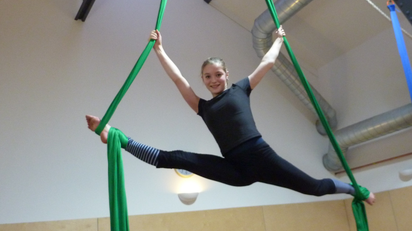 Female Youth in the air on a green aerial silk doing the splits