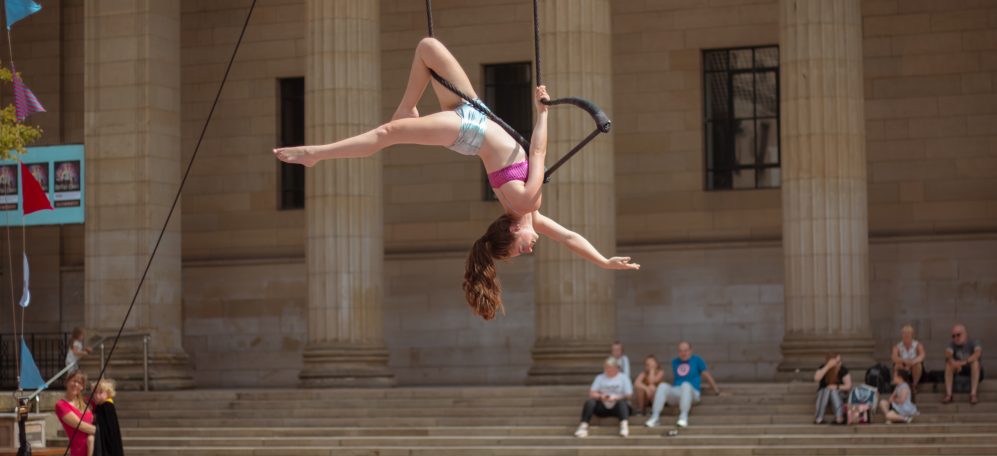 An image of a woman suspended on a trapeze outside to show off aerial arts