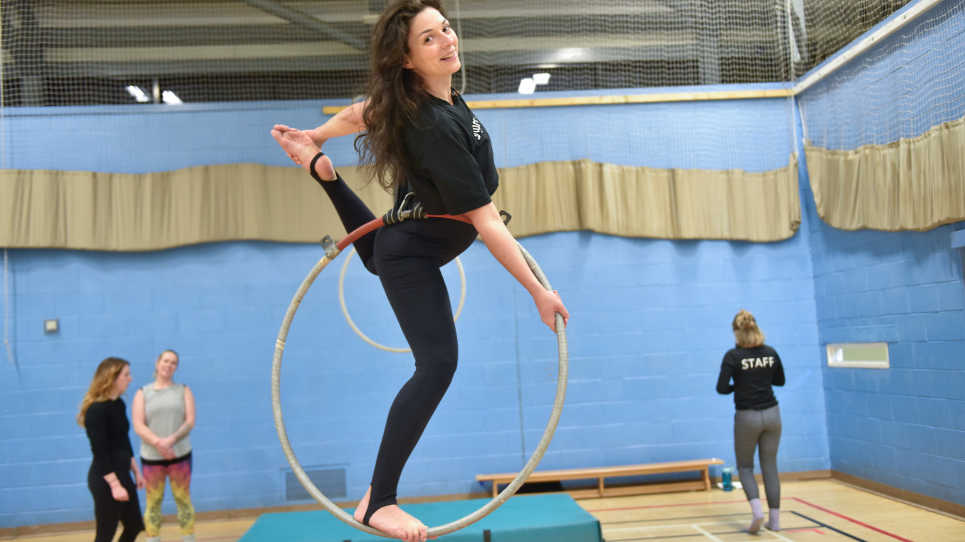 An aerial student in an arabesque position standing in an aerial hoop
