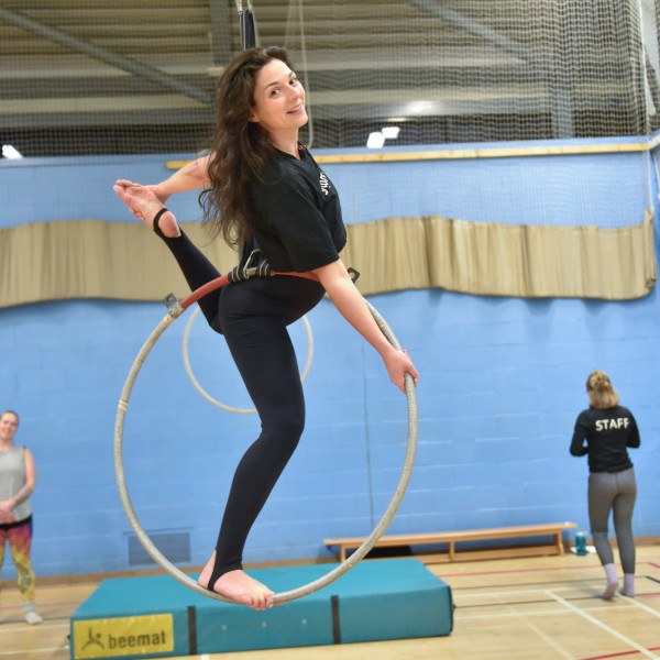 An aerial student in an arabesque position standing in an aerial hoop