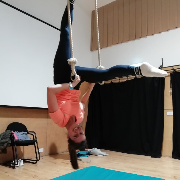 Smiling woman in L-hang pose on trapeze