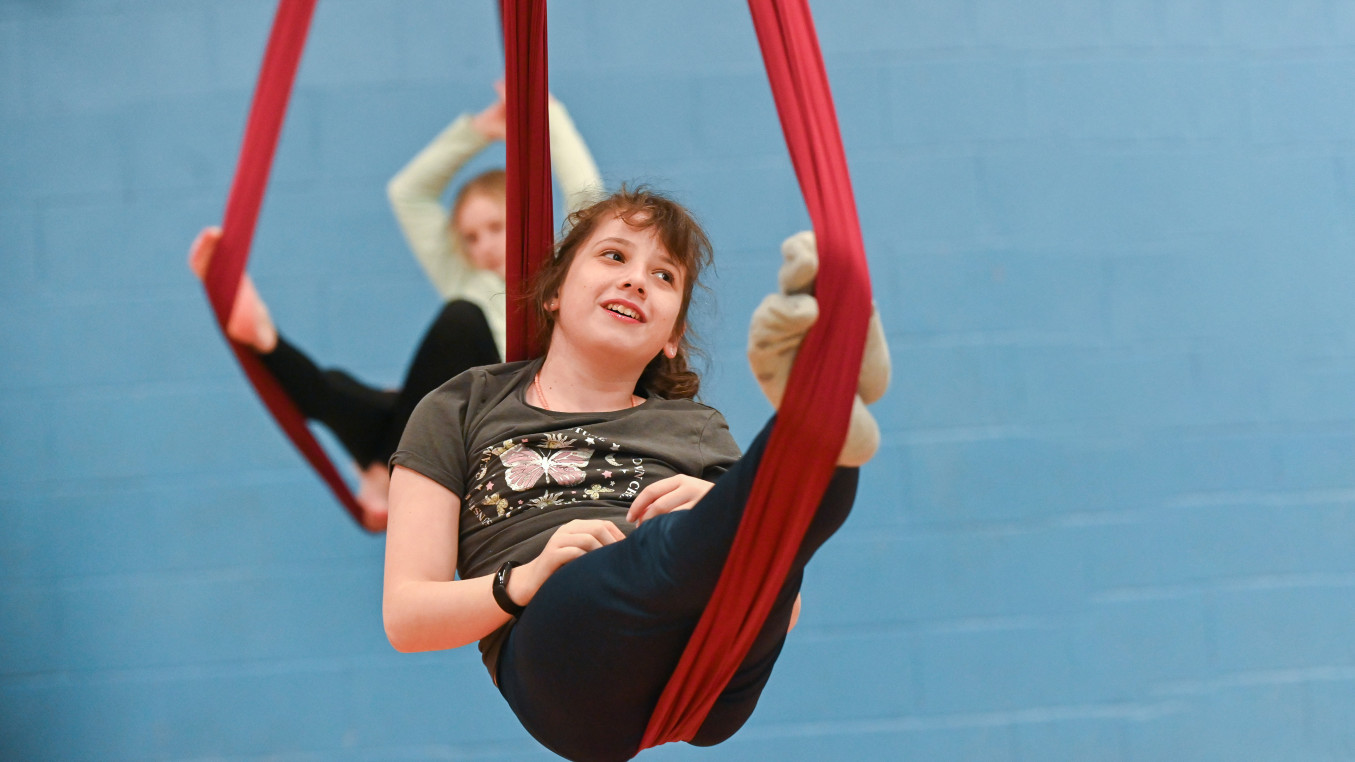 A young person in a cradle position on an aerial silks hammock