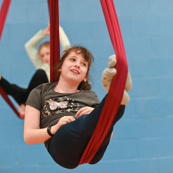 A young person in a cradle position on an aerial silks hammock