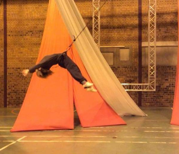 Chrissie is soaring backwards suspended by a harness, she appears to be moving fast and is in an arch with her body arms overhead.