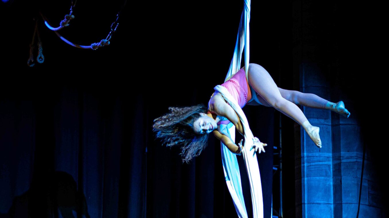 Single aerialist wrapped in white aerial silk in hip-lock position on a stage