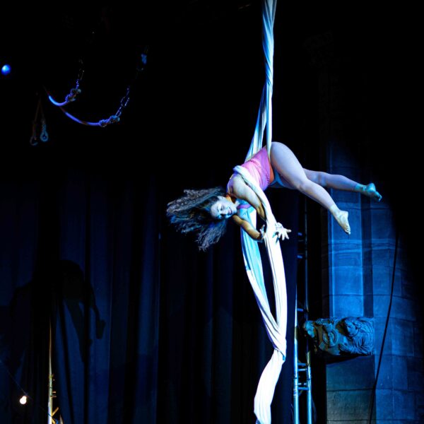 Single aerialist wrapped in white aerial silk in hip-lock position on a stage